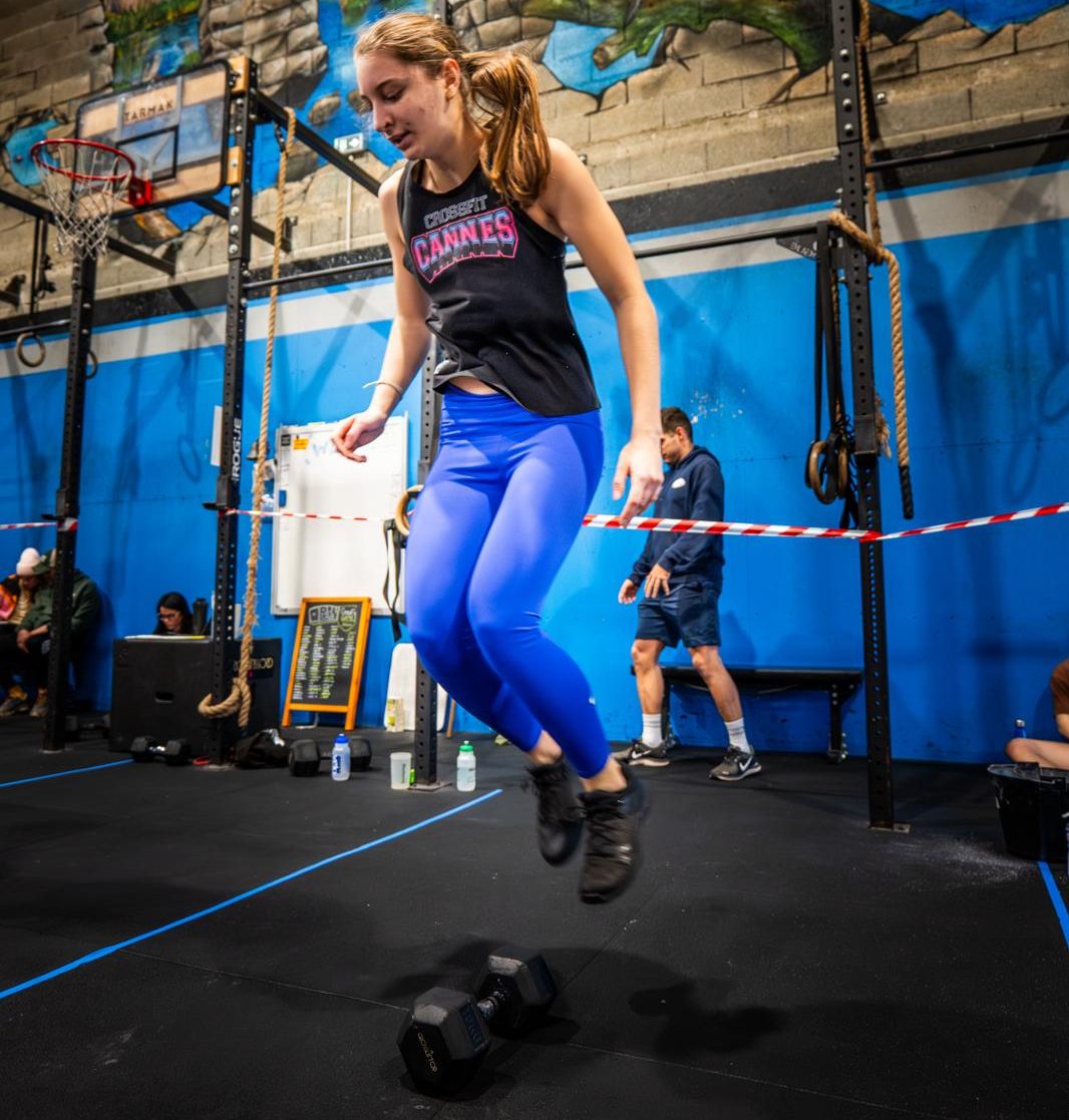 jeune femme sportive saute par dessus un haltère pendant un cours de coaching personnalisé